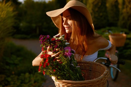Charming lady smelling wildflower blossoms during bicycle walk in park on weekend. Feminine, tenderness and charm of youth