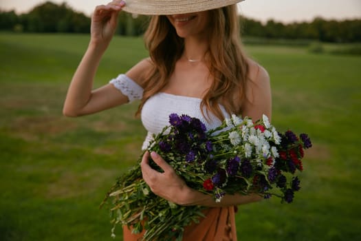 Beautiful woman holding bunch of wildflower standing over green countryside field. Femininity, natural beauty and innocence concept