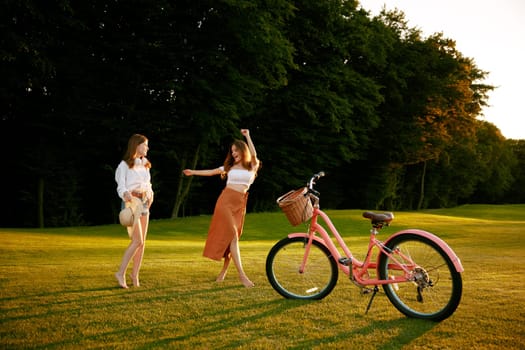 Women friends walking on forest lawn taking break from their cycling workout routine. Young hipster female teenagers spending time on weekend vacation