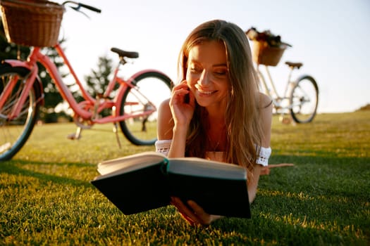 Closeup portrait of young woman reading book on nature taking break during bicycle travel outdoors. Relaxed time, hobby recreation activity
