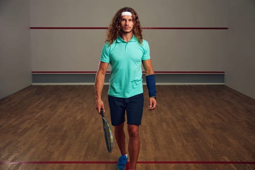 Portrait of man holding squash racquet walking among sport court. Confident racquetball player and professional sport