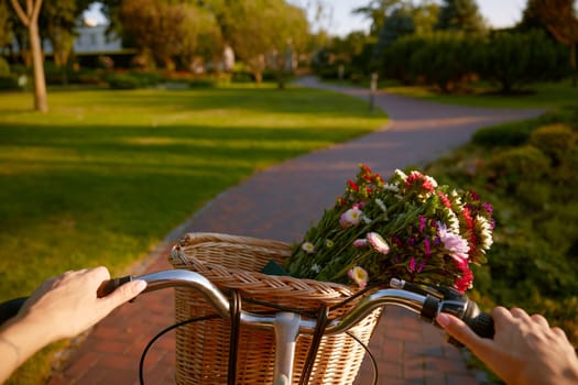 Closeup woman riding vintage bicycle with wildflower bouquet in basket. Handlebar view
