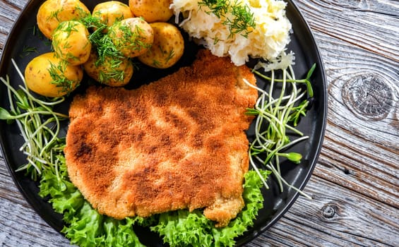 Pork breaded cutlet coated with breadcrumbs served with potatoes and cabbage