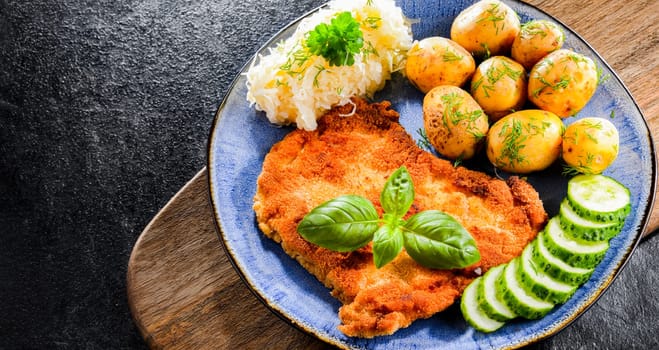 Pork breaded cutlet coated with breadcrumbs served with potatoes and cabbage