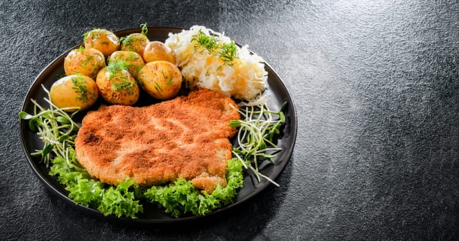 Pork breaded cutlet coated with breadcrumbs served with potatoes and cabbage