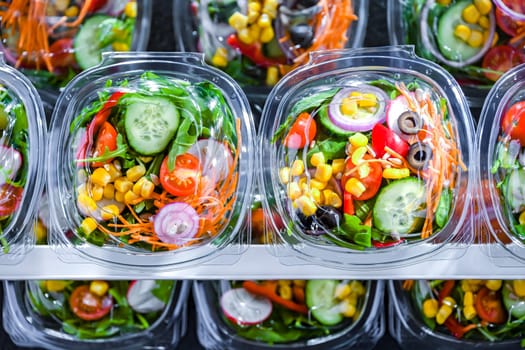 Plastic boxes with pre-packaged vegetable salads, put up for sale in a commercial refrigerator