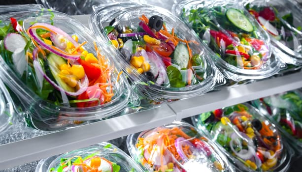 Plastic boxes with pre-packaged vegetable salads, put up for sale in a commercial refrigerator
