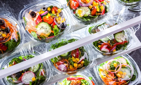 Plastic boxes with pre-packaged vegetable salads, put up for sale in a commercial refrigerator