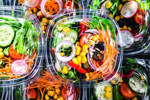Plastic boxes with pre-packaged vegetable salads, put up for sale in a commercial refrigerator