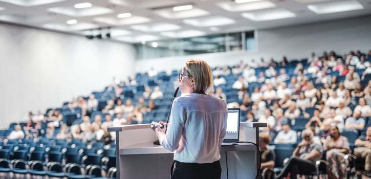 Female speaker giving a talk on corporate business conference. Unrecognizable people in audience at conference hall. Business and Entrepreneurship event