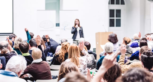 I have a question. Group of people sitting at the chairs in conference hall, raising their hands. Workshop at university. Business and Entrepreneurship event.