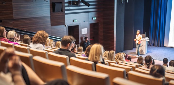 Speaker giving a talk in conference hall at business event. Rear view of unrecognizable people in audience at the conference hall. Business and entrepreneurship concept