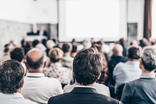 Speaker giving a talk in conference hall at business event. Audience at the conference hall. Business and Entrepreneurship concept. Focus on unrecognizable people in audience.