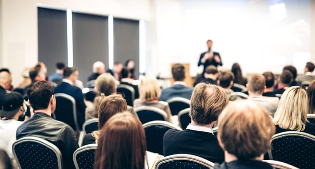Speaker giving a talk in conference hall at business event. Rear view of unrecognizable people in audience at the conference hall. Business and entrepreneurship concept