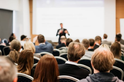 Speaker giving a talk in conference hall at business event. Rear view of unrecognizable people in audience at the conference hall. Business and entrepreneurship concept