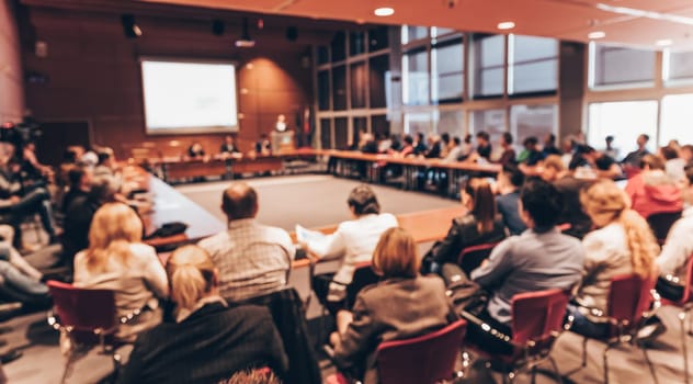 Speaker giving a talk on corporate business event. Audience at the conference hall. Business and Entrepreneurship event. Focus on unrecognizable business people in the rear.