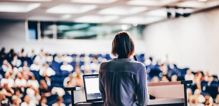 Female speaker giving a talk on corporate business conference. Unrecognizable people in audience at conference hall. Business and Entrepreneurship event