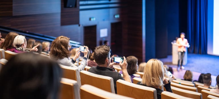 Speaker giving a talk in conference hall at business event. Rear view of unrecognizable people in audience at the conference hall. Business and entrepreneurship concept