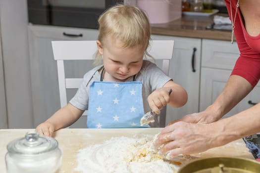 Cute blond little child boy is helpful in making the dough in domestic kitchen.  Home baking Christmas cookies concept.