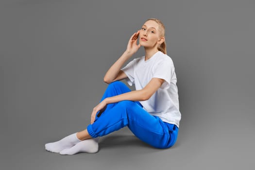 Young sportive woman sitting on the floor on solid grey background