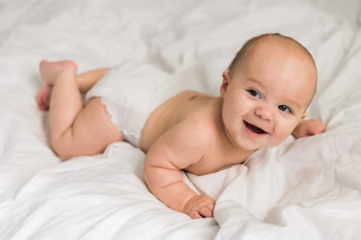 Smiling newborn baby on a white bed at home, the concept of a happy healthy infant baby. Generation alpha and gen alpha.