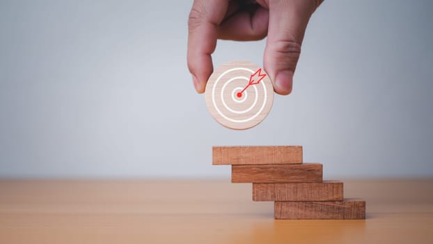 Businessman's hands hold a circular wooden board with a dartboard. It represents the concept of business strategy and target action plan.