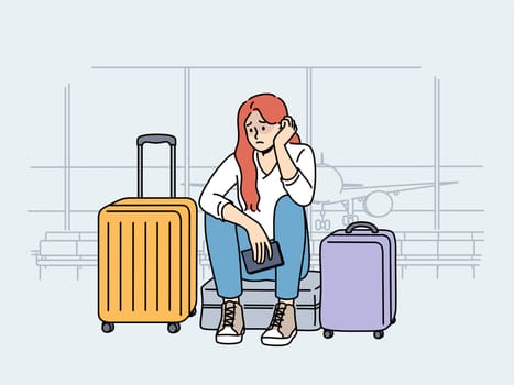 Upset woman airport passenger sits among tourist suitcases and waits for plane that is late due to bad weather. Concept of flight cancellation causing inconvenience to airport passengers