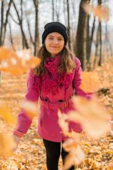Smiling positive young woman throws up the yellow autumn leaves in the forest at sunset