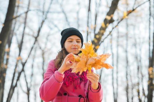 Young woman in a hat collects autumn leaves. Fall season concept. Generation Z and gen z youth.