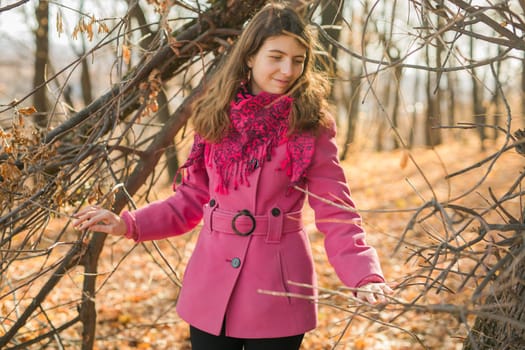 Cheerful young woman with pink scarf relaxing at park with yellow trees in background. Smiling beautiful girl enjoying warm sunny weather in autumn season. Happy pretty natural woman laughing in fall season