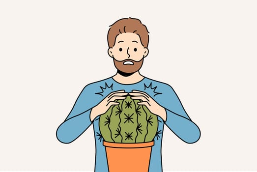 Man is scared and touches cactus and gets wound for concept of problems associated with unshaven hair and need for depilation. Funny stupid guy pricked himself touching cactus in pot