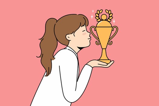 Little girl leader kisses golden cup won in school olympiad or sports competition. Schoolgirl leader with trophy received for achievements in education or outstanding athletic skills