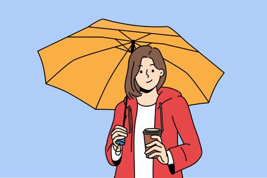 Woman holds plastic cup with coffee takeouts and umbrella protecting from rain during autumn walk. Girl enjoys taste of invigorating takeouts coffee and looks at screen with thoughtful grin.