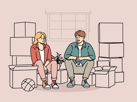 Couple sits among boxes of belongings after moving into new house and rejoices at improvement in living conditions thanks to mortgage. Man and woman took out mortgage loan to buy apartment