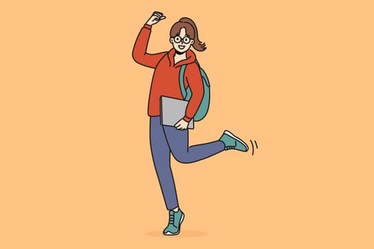 Cheerful student girl makes victory gesture and holds books in hands, rejoicing at receiving quality education. Young woman student with backpack smiling celebrating entering college or university