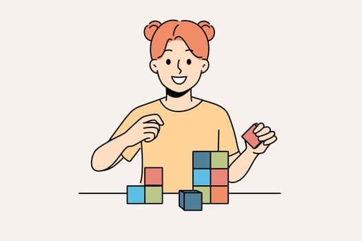 Happy little girl playing with wooden child cubes standing at table and smiling looking at screen. Child plays educational game that helps improve intellectual abilities and fine motor skills.