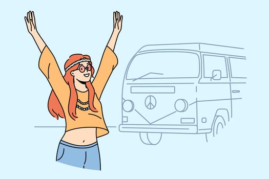 Teenage hippie girl goes on summer travel in minivan and raises hands, rejoicing at opportunity to relax. Young hippie woman standing near tourist van for travel with pacifism symbol
