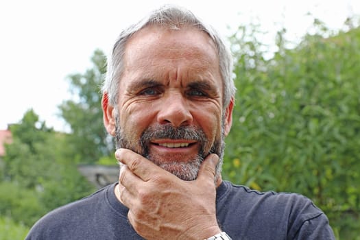 A man with gray hair and a beard laughs into the camera