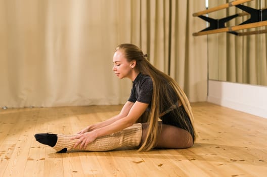 Young woman ballerina stretching and training at barre in dance studio - ballet and dancer