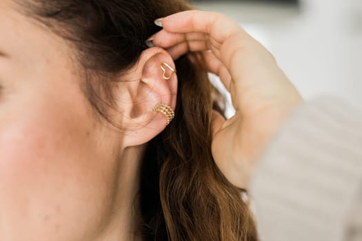 Cropped close-up shot of a young woman with two asymmetrical golden ear cuffs. Female with golden ear cuffs, side view