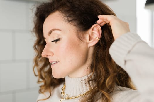 Cropped close-up shot of a young woman with two asymmetrical golden ear cuffs. Female with golden ear cuffs, side view