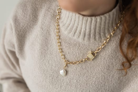 Close-up female in modern gold metal necklace chain with pearl pendant.