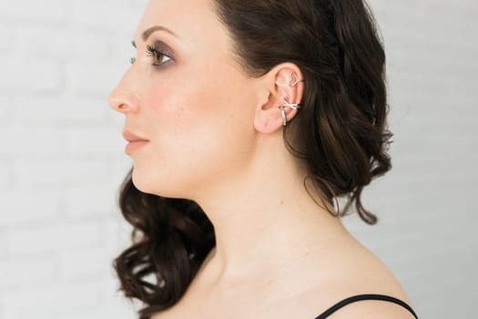 Cropped close-up shot of a young woman with asymmetrical silver ear cuffs. Female with metal ear cuffs, side view.