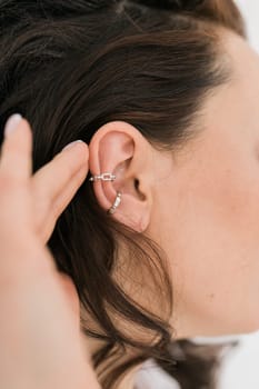 Cropped close-up shot of a young woman with asymmetrical silver ear cuffs. Female with metal ear cuffs, side view.