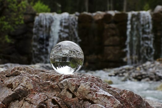 A glass sphere reflects a waterfall in the mountains
