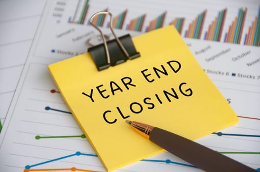 Year End Closing text on sticky note with statistic and graph background.