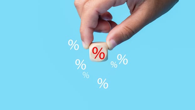 Human hand holds discount percentage sign icon on light blue background represents online shopping concept, special price products and promotions.