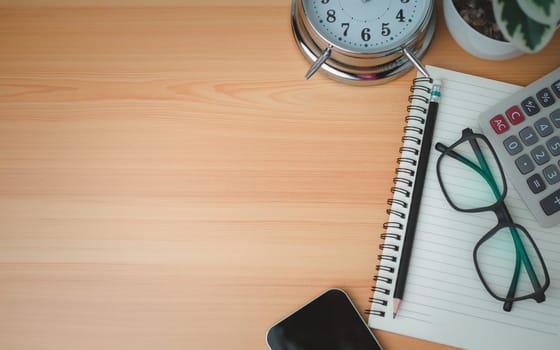 Office table of modern workplace with notebooks and pencils, phone, clock on wooden table. side view and copy space on wooden floor, Flat lay, side view office table with glasses and calculator.