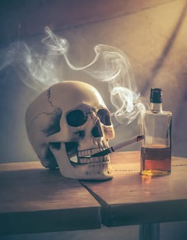 Skull smoking a cigarette with an alcohol bottle near on the table. Toxic addictions concept, tobacco smoke and spirit drinking health risk