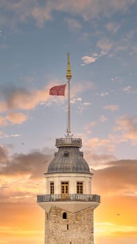 The Maiden's Tower or Kiz Kulesi, an iconic landmark in Istanbul, Turkey, is captivating in the warm hues of a setting sun. The vibrant Turkish flag flutters atop the tower